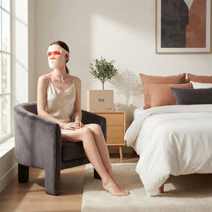 A woman wearing a professional LED red light mask while relaxing in a modern, sunlit bedroom with terracotta and charcoal dec